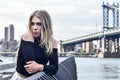 Outdoor portrait of young blond sensual woman posing in elegant clothes on the pier with Manhattan Bridge on the background. Royalty Free Stock Photo