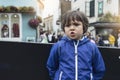 Outdoor portrait of young boy standing alone on street with with blurry background of people, Dramatic portrait of Kid with angry Royalty Free Stock Photo