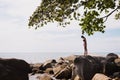 Outdoor portrait of young elegant fit woman standing on a rock near tropical beach with sea. Sports girl in bikini enjoy Royalty Free Stock Photo