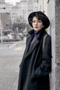 Outdoor portrait of young fashionable lady in trendy hat, black classic coat, posing on the street of a European city. Royalty Free Stock Photo