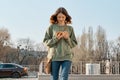 Outdoor portrait of young girl 15 years walking, reading text message on smartphone, spring sunny day background Royalty Free Stock Photo