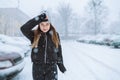 Outdoor portrait of young woman on street under snowfall. Bad cold weather, windy winter. Woman try to hide her face