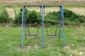 Outdoor public playground equipment metal swing with rusted frame and dilapidated wooden seats