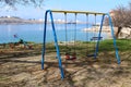 Outdoor public playground equipment in shape of swing and seesaw surrounded with grass and public bench with industrial complex