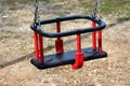 Outdoor public playground equipment strong plastic red and black swing seat with safety frame for small children and connected Royalty Free Stock Photo