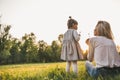 Outdoor rear view of happy girl kid playing with her mother outside. Portrait of woman and her cute child blowing dandelion in the Royalty Free Stock Photo