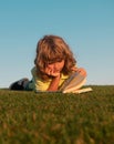 Outdoor school, motivation learning kids. Child boy is reading a book on the spring park. Relaxing on the grass in the Royalty Free Stock Photo