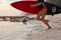 Outdoor shot of active fitness girl carries surfboard, prepares for surfing trip, stands on sandy beach near water Royalty Free Stock Photo