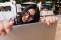 Outdoor shot of black-haired girl working with computer. Portrait of ecstatic tanned lady using lap