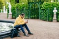 Outdoor shot of hipster guy with beard dressed stylish resting in park near fountain surfing social networks using his cell phone Royalty Free Stock Photo