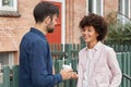 Outdoor shot of mixed race woman and man meet at street, stand near hence and brick building, have pleasant talk with