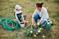 Outdoor shot of mother planting young raspberry plant with her cute little helping hand, family holding raspberry and flowers,