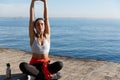 Outdoor shot of relaxed young woman meditating near the sea, practice yoga, sitting in asana on a wooden pier floor Royalty Free Stock Photo