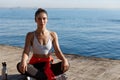 Outdoor shot of relaxed young woman meditating near the sea, practice yoga, sitting in asana on a wooden pier floor Royalty Free Stock Photo