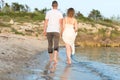 Outdoor shot of romantic young couple walking along the sea shore holding hands. Royalty Free Stock Photo