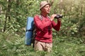 Outdoor shot of senior man with backpack and rug, holding binoculars, looking far away in forest, enjoying beautiful nature, male Royalty Free Stock Photo