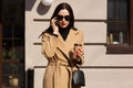 Outdoor shot of serious lovely attractive model poses over local restaurant, holding phone in her hand, having important