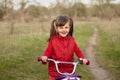 Outdoor shot of smiling happy little girl wearing red casual shirt, kid expressing happiness, playing in meadow on green grass, Royalty Free Stock Photo