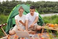 Outdoor shot of young family sitting on ground near tent and using laptop, man pointing at notebook screen with shocked expression Royalty Free Stock Photo