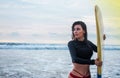 Outdoor shot of young girl waxes surfboard for safe riding waves, dressed in black swimsuit, takes care of safety, with white Royalty Free Stock Photo