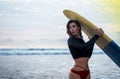 Outdoor shot of young girl waxes surfboard for safe riding waves, dressed in black swimsuit, takes care of safety, with Royalty Free Stock Photo