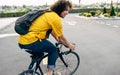 Young man smiling and wearing yellow shirt with backpack and his bike walking in the city street. Male courier with curly hair Royalty Free Stock Photo