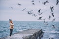 Outdoor side view image of young woman at the ocean enjoying the journey. Pretty female watching flying seagulls by the sea on the