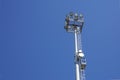 Outdoor stadium lights and telecommunication tower against daytime blue sky. Royalty Free Stock Photo