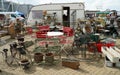 Outdoor stall at antique fair with pots and garden furniture caravan in background.