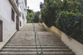 Outdoor steps climbing up with building on one side and plants on the other. Metal railings in the middle