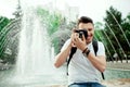 Closeup portrait of handsome young man taking photo in city park. Stylish boy in a white tshirt, with bagpack taking photos Royalty Free Stock Photo