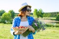 Outdoor summer portrait of an adult woman with strawberries, bouquet of wildflowers, straw hat and sunglasses. Nature background, Royalty Free Stock Photo