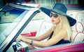 Outdoor summer portrait of stylish blonde vintage woman driving a convertible red retro car. Fashionable attractive fair hair girl Royalty Free Stock Photo