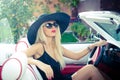 Outdoor summer portrait of stylish blonde vintage woman driving a convertible retro car. Fashionable attractive fair hair female Royalty Free Stock Photo
