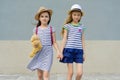 Outdoor summer portrait of two happy girl friends 7, 8 years holding hands. Girls in striped dresses, hats with backpack, Royalty Free Stock Photo