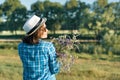 Outdoor summer portrait of woman with bouquet of wildflowers, straw hat. View from the back, nature background, rural landscape,