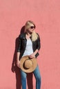 Outdoor summer portrait of young blonde woman in black leather jacket and white t shirt with sunglasses hold hat in hands against Royalty Free Stock Photo