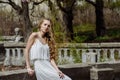 Outdoor summer portrait of young pretty cute girl. Beautiful woman posing at old bridge. in white dess standing near stone railin Royalty Free Stock Photo