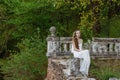 Outdoor summer portrait of young pretty cute girl. Beautiful woman posing at old bridge. in white dess siting near stone railing. Royalty Free Stock Photo