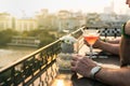 Outdoor table in a cafe and bar with an orange cocktail and man hands closeup. Urban cityscape and lake on background. Brilliant s