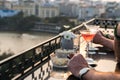 Outdoor table in a cafe and bar with an orange cocktail and man hands closeup. Urban cityscape and lake on background. Brilliant s