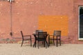 Outdoor table and chairs in front of an artsy looking old salmon color painted brick wall