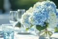 Outdoor table setting with blue hydrangea bouquet on white tablecloth. Elegant dinnerware and wine glasses in harmony with garden Royalty Free Stock Photo
