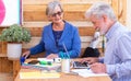 Outdoor in the terrace a rustic wooden office with a couple of senior people with white hair sitting and working with laptop and