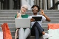 African and Muslim women sitting on the steps of mall with laptop and tablet and shopping online.