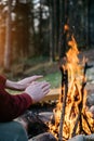 Outdoor vertical image of traveler warming his hands by near campfire an in forest. Royalty Free Stock Photo