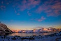 Outdoor view of gorgeous sunset over mountain peaks coevered with snow and partial frozen lake in Svolvaer