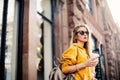 Outdoor waist up portrait of young beautiful woman with long hair. Model wearing stylish sunglasses, clothes, holding bag. City li