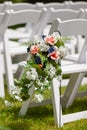 Outdoor wedding ceremony artificial flowers by white chairs