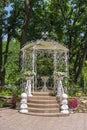 Outdoor white metal gazebo with roof in a garden against green trees